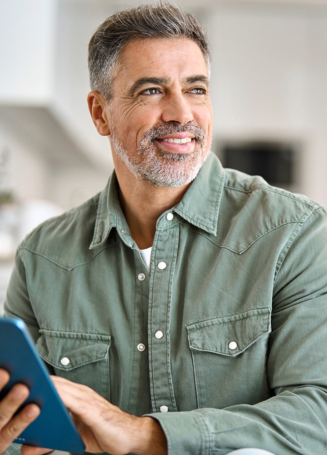 Smiling man holding a tablet in a kitchen.