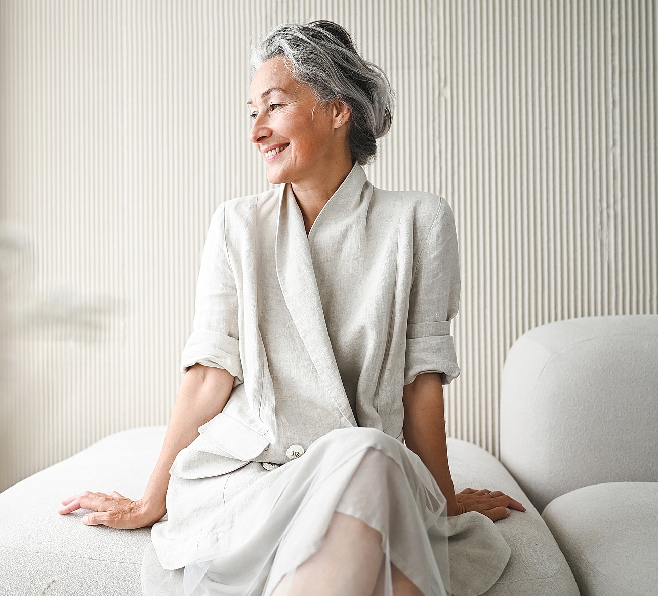 Smiling woman in elegant linen attire, sitting.